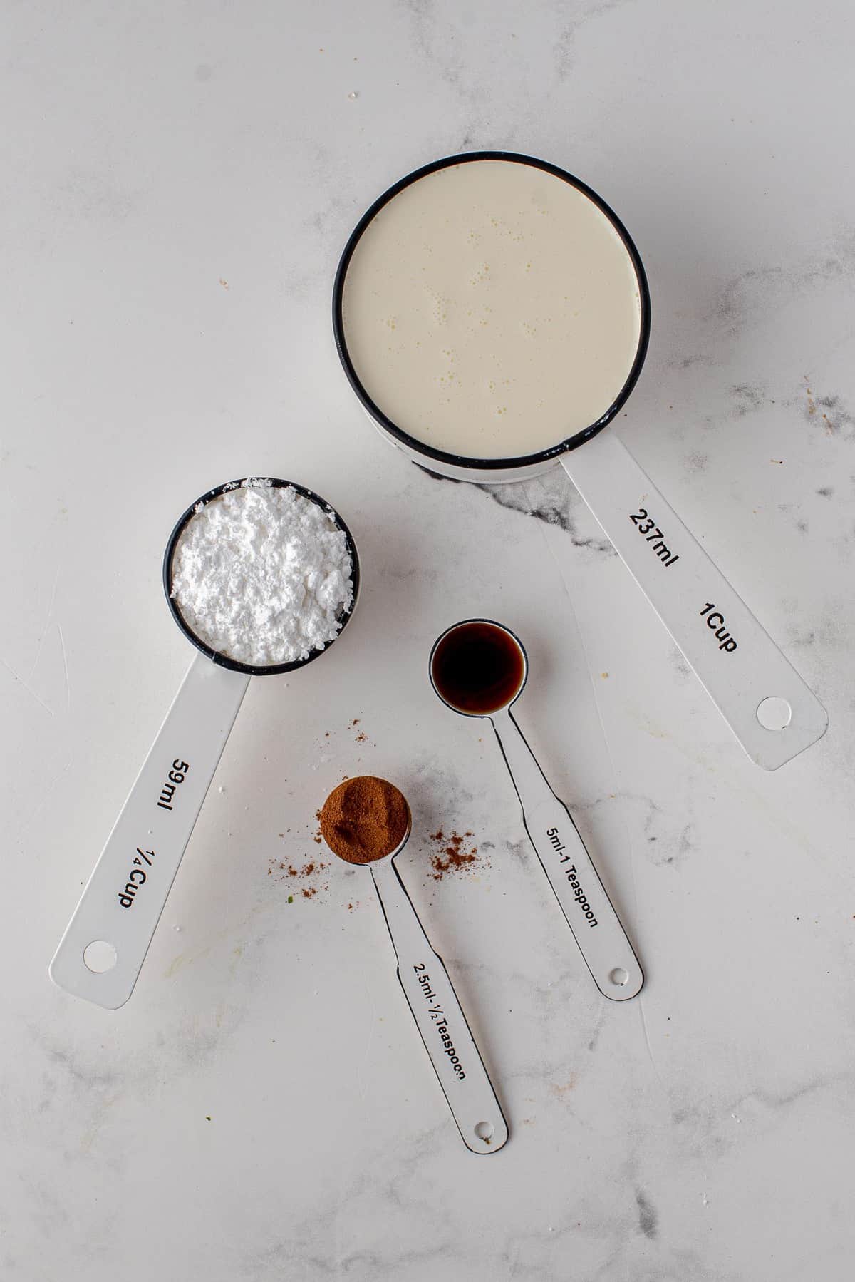 Crème, sucre glace, cannelle et vanille dans des ustensiles de mesure.