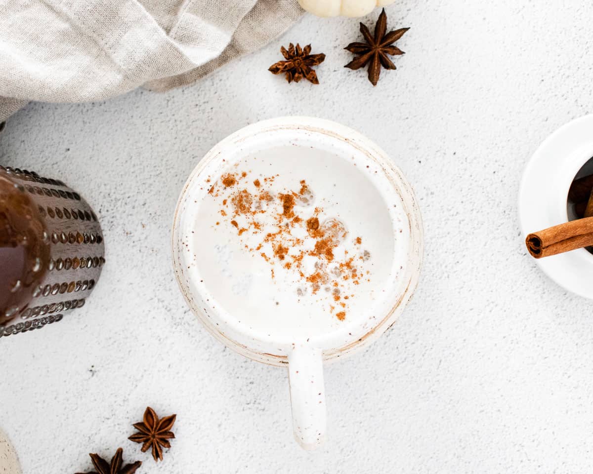 Un latte dans une tasse blanche sur un fond blanc, décoré d'un mélange d'épices incluant de la cannelle.