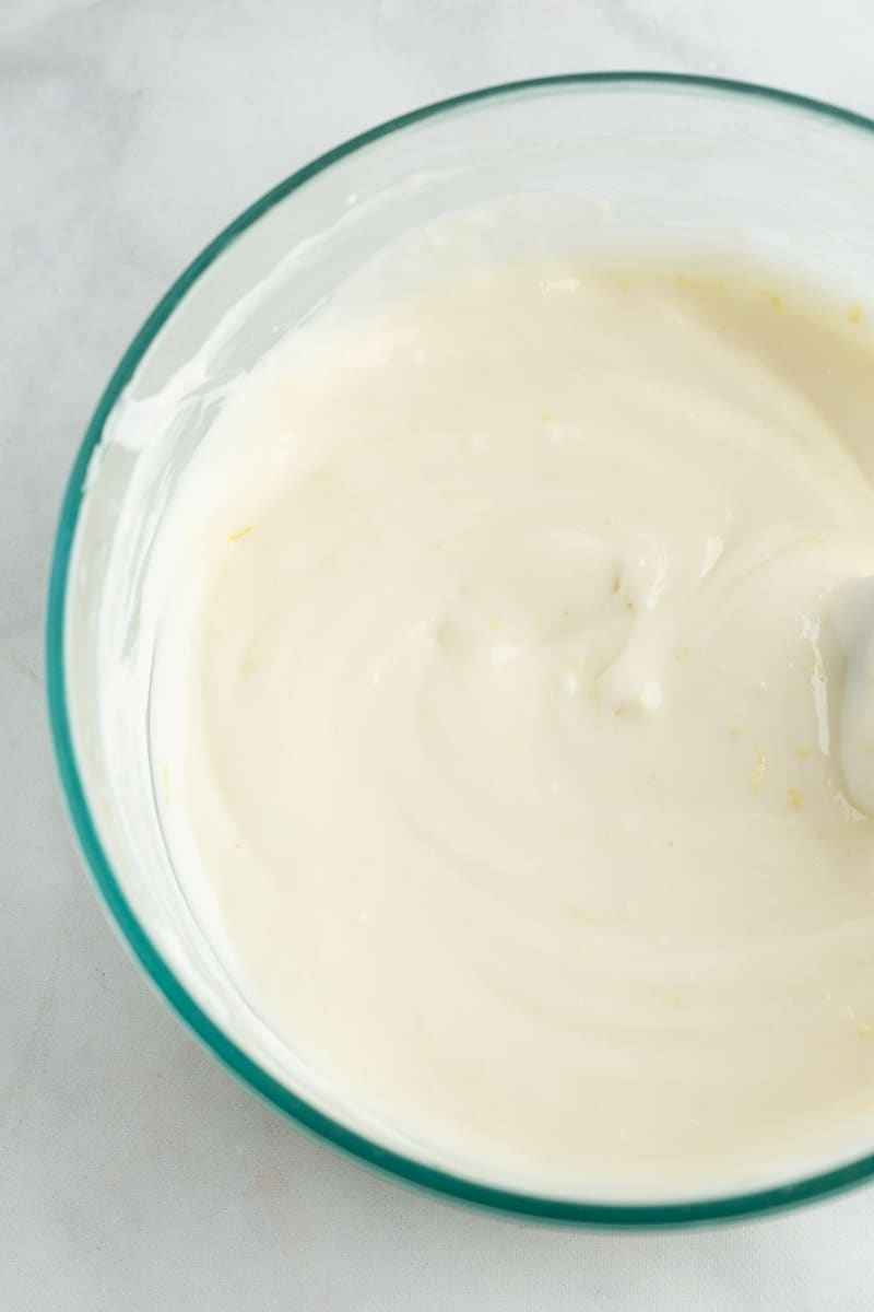 Glaçage au citron et au fromage frais dans un bol en verre sur fond blanc.