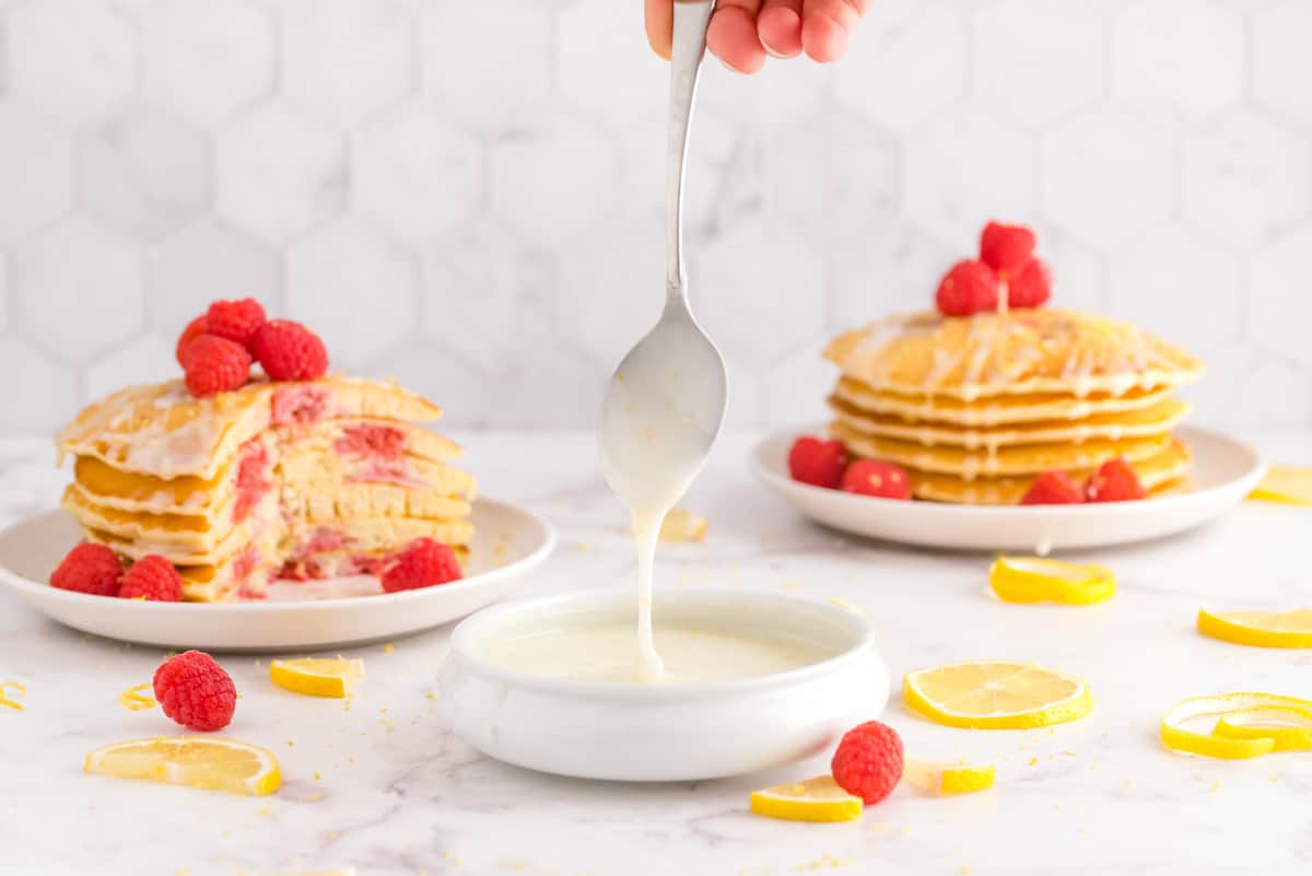 Glaçage dans un petit bol, pancakes en arrière-plan. Citrons et framboises également visibles.