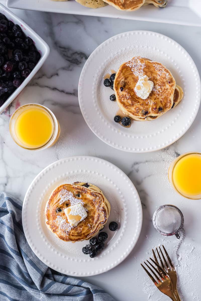 Vue d'ensemble d'un petit-déjeuner pour deux composé de pancakes, de myrtilles et de jus d'orange.