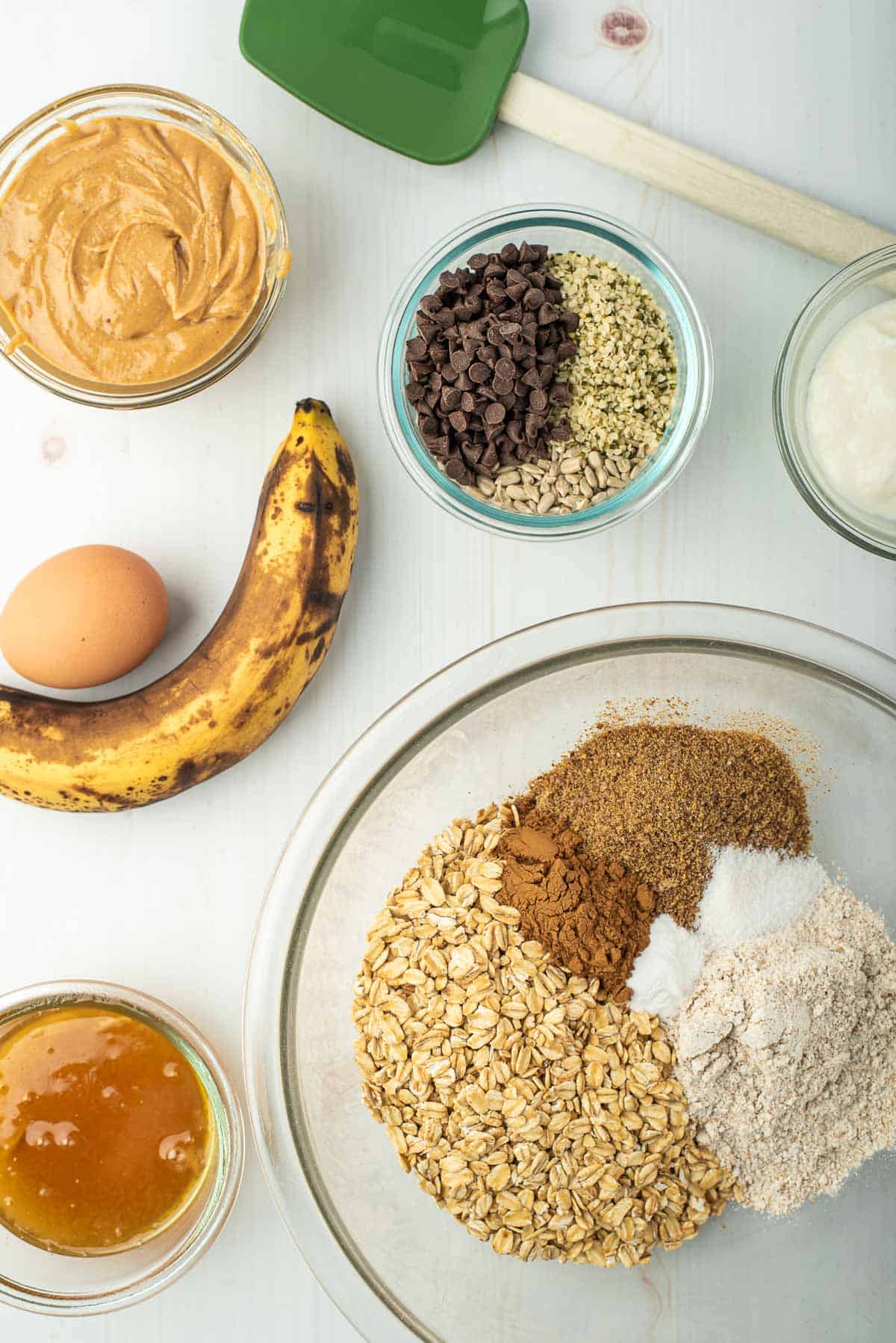 Ingrédients secs pour cookies de petit déjeuner dans un bol, entourés d'ingrédients supplémentaires.