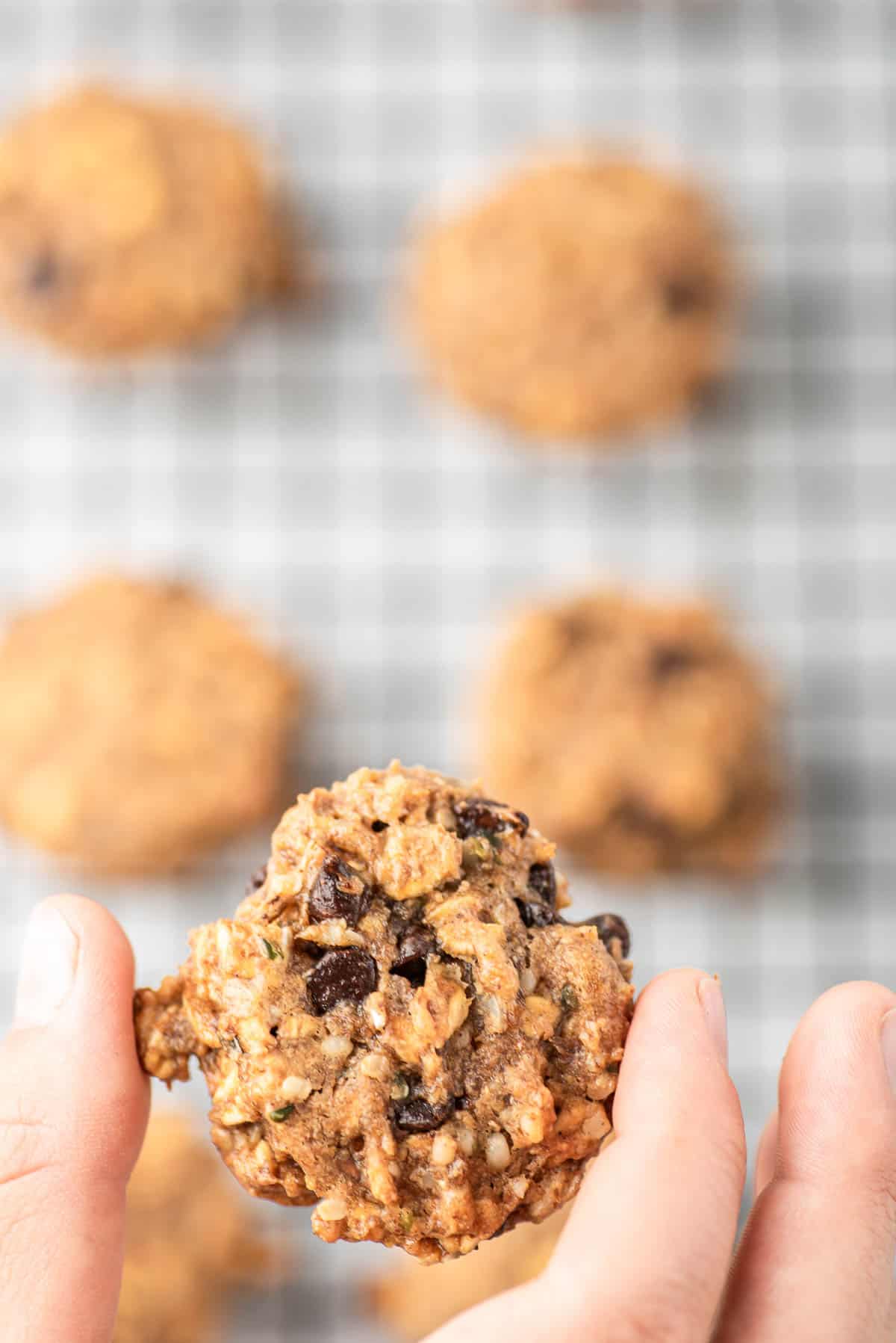 Une main tenant un cookie de petit déjeuner au-dessus d'autres cookies.