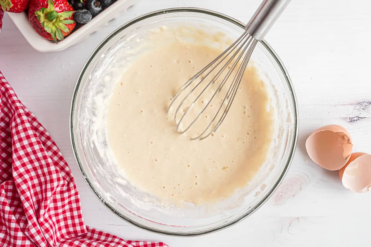 Pâte à pancakes et fouet en métal dans un bol transparent.