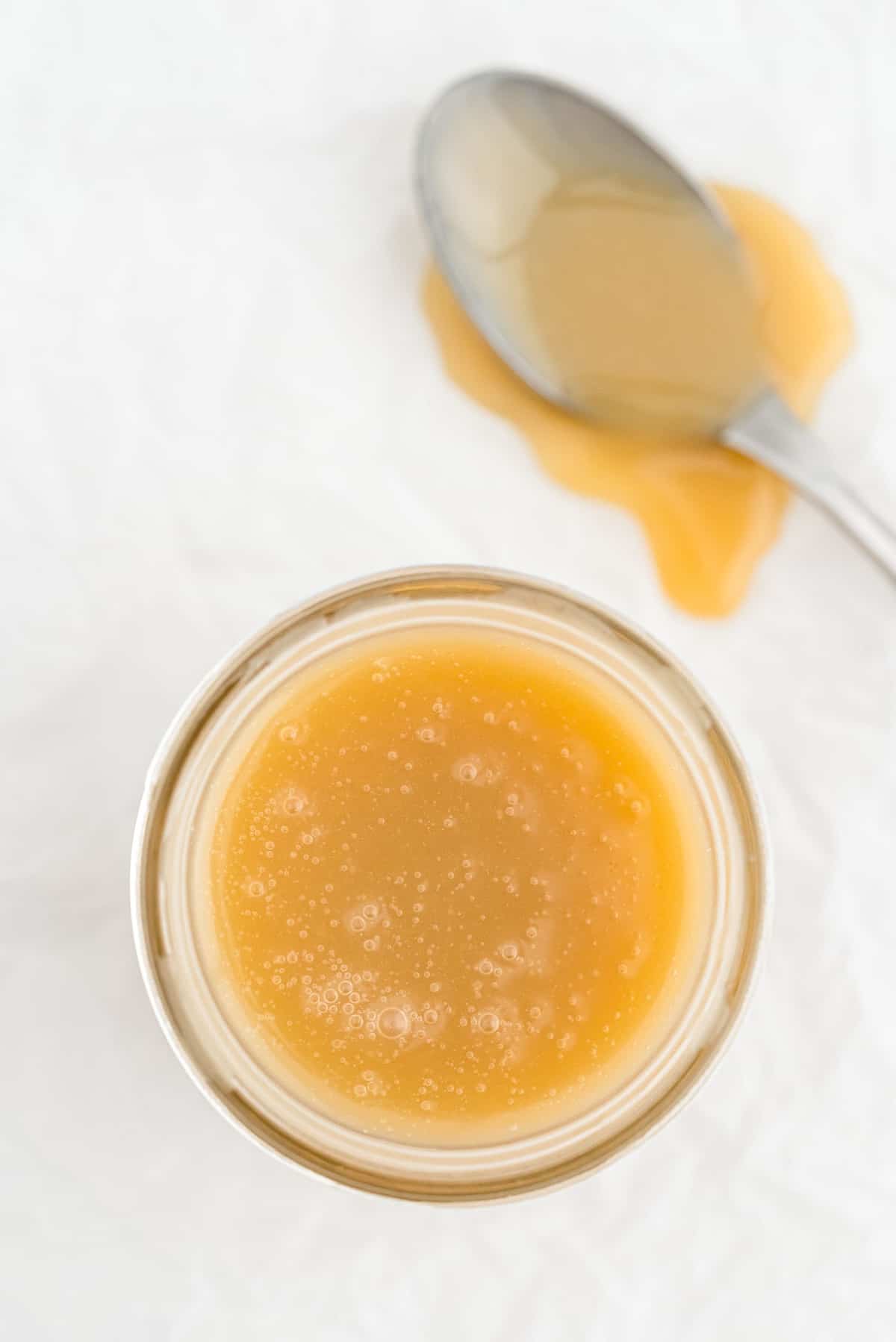 Pot de sauce caramel sur une surface gris clair, une cuillère à côté couverte de caramel.