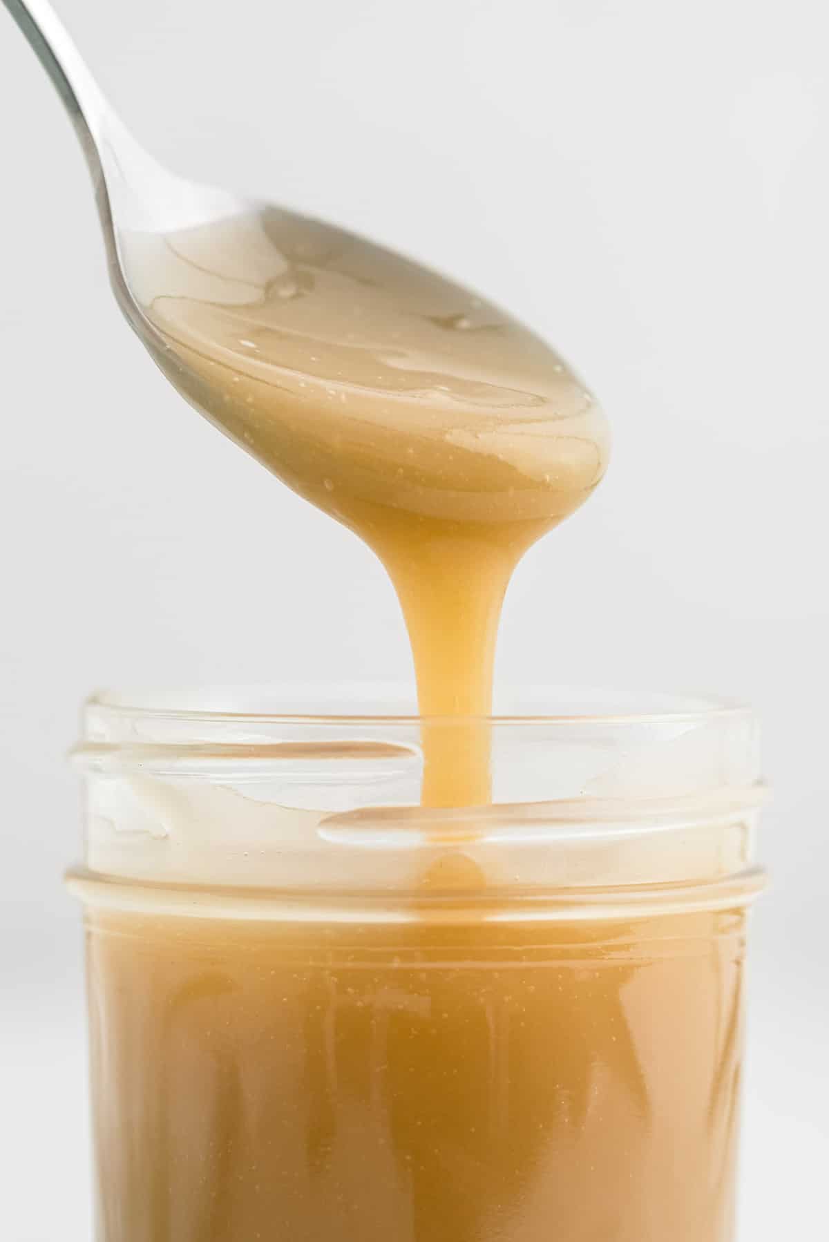 Gros plan sur du caramel coulant d'une cuillère dans un pot.