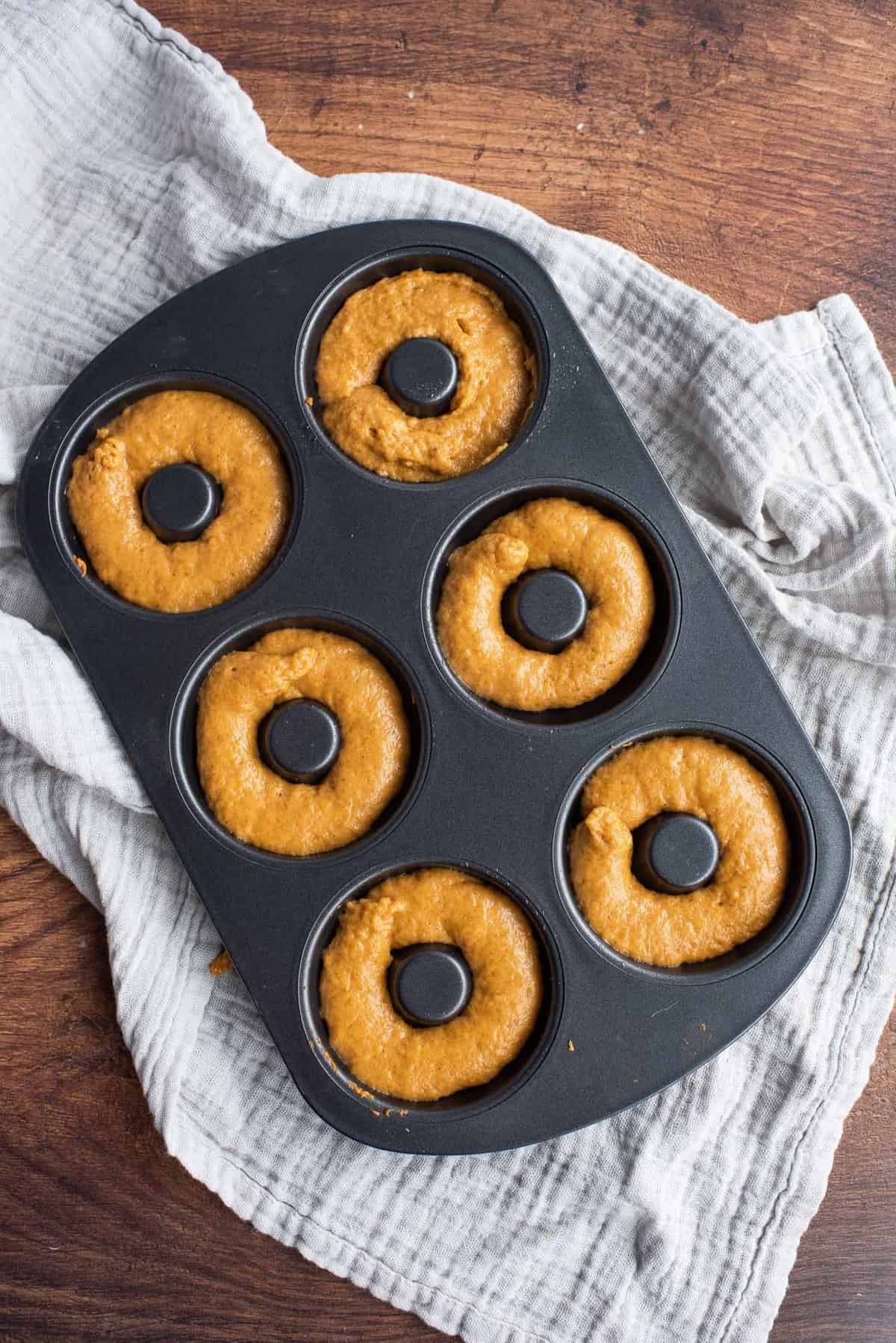Donuts à la citrouille non cuits dans un moule à donuts noir.