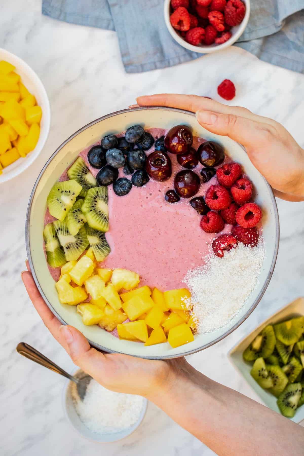 Bol de smoothie arc-en-ciel tenu entre deux mains.