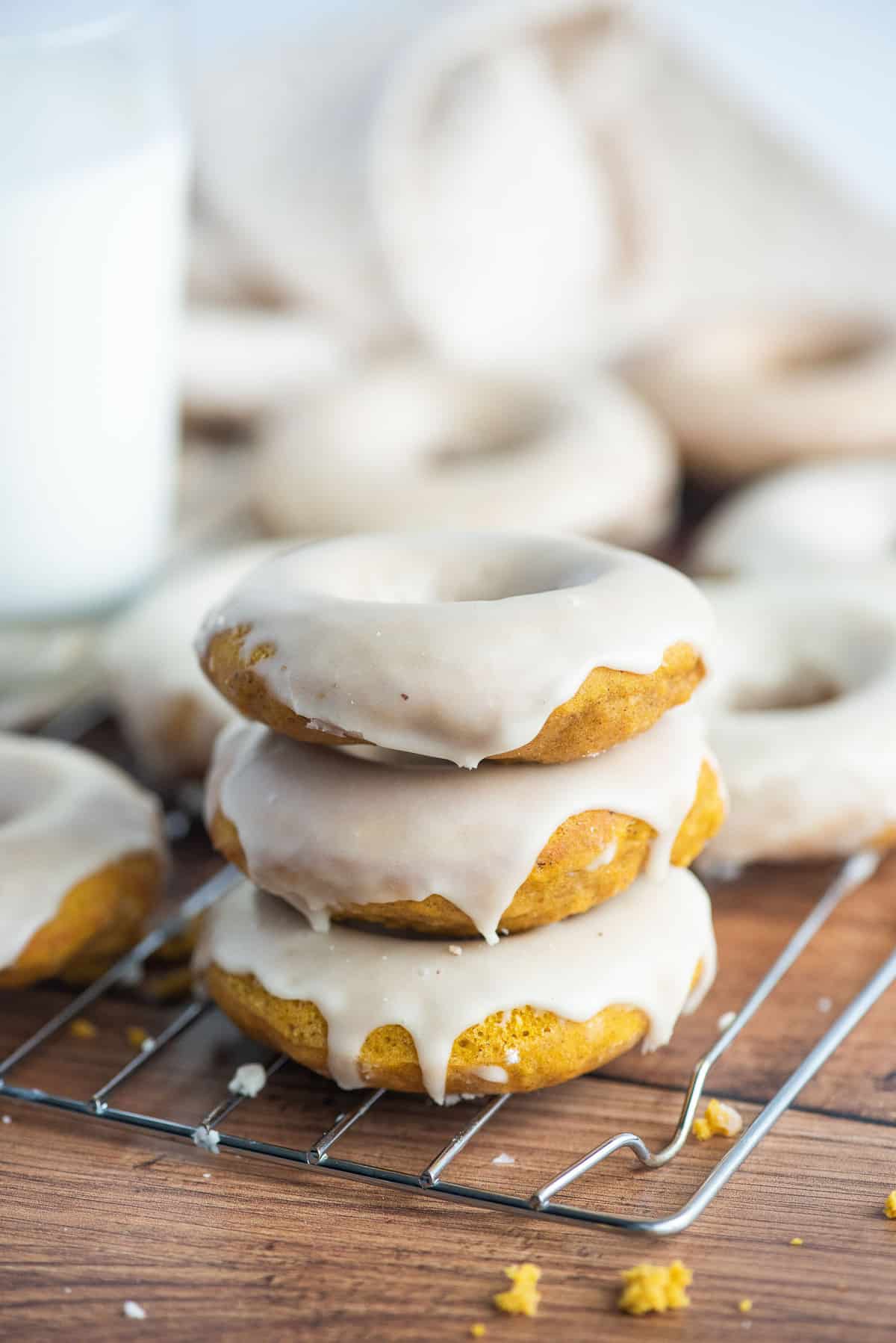 Trois donuts à la citrouille avec glaçage, d'autres en arrière-plan.
