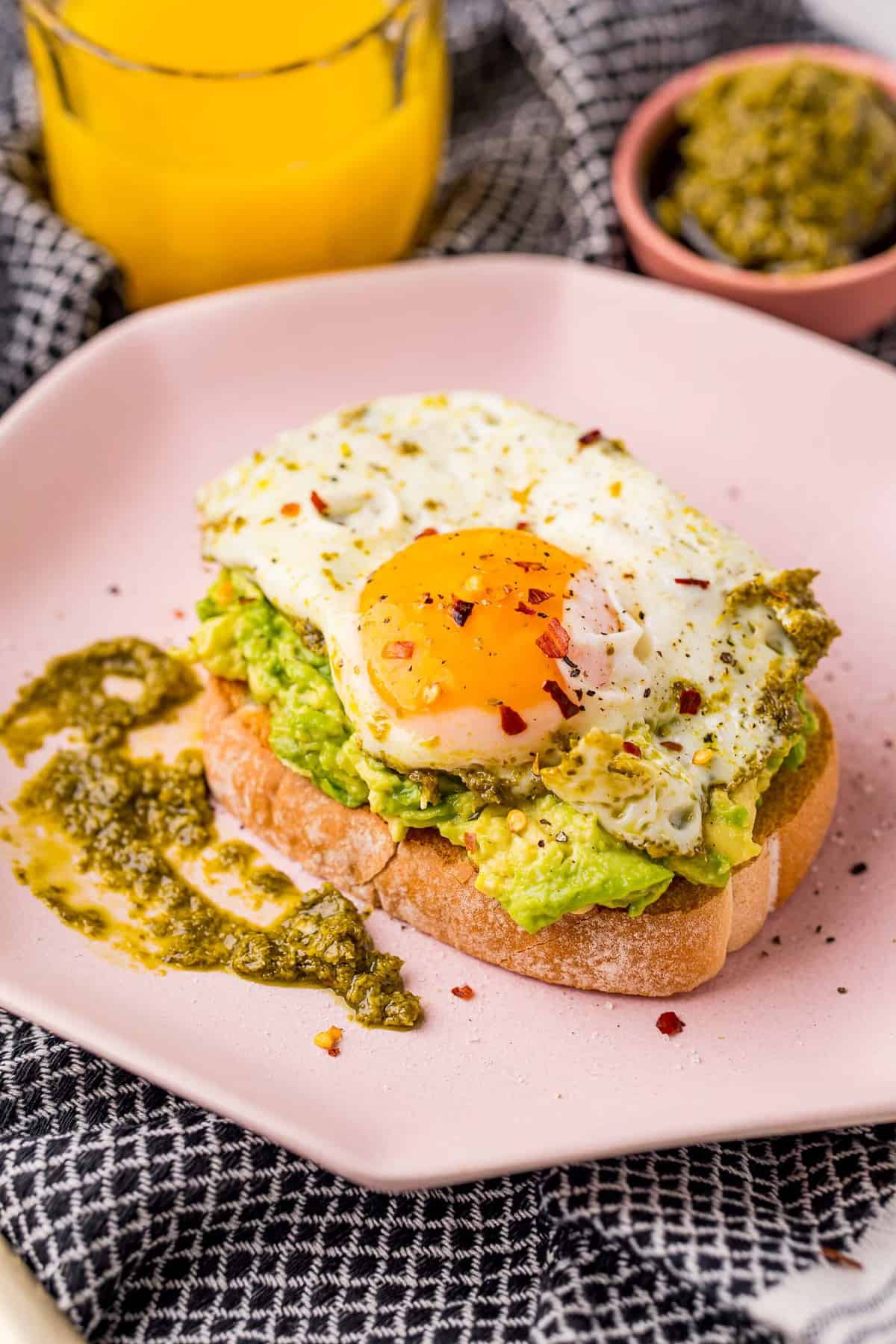 Œuf cuit avec pesto sur une tartine d'avocat dans une assiette rose.