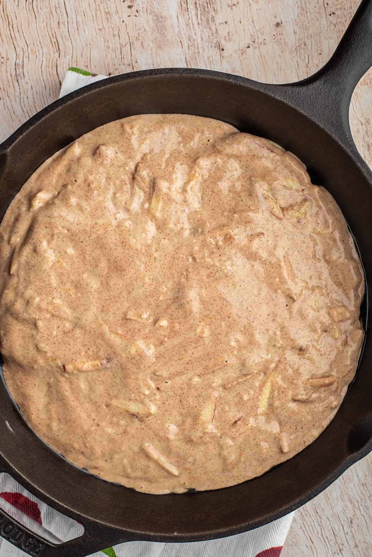 Pâte de pancake aux pommes et à la cannelle dans une grande poêle en fonte noire.