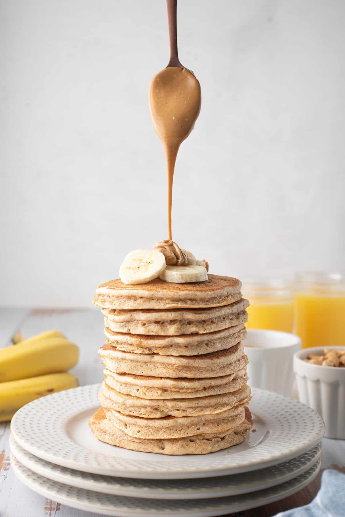 Du beurre de cacahuète versé d'une cuillère sur une très grande pile de pancakes.