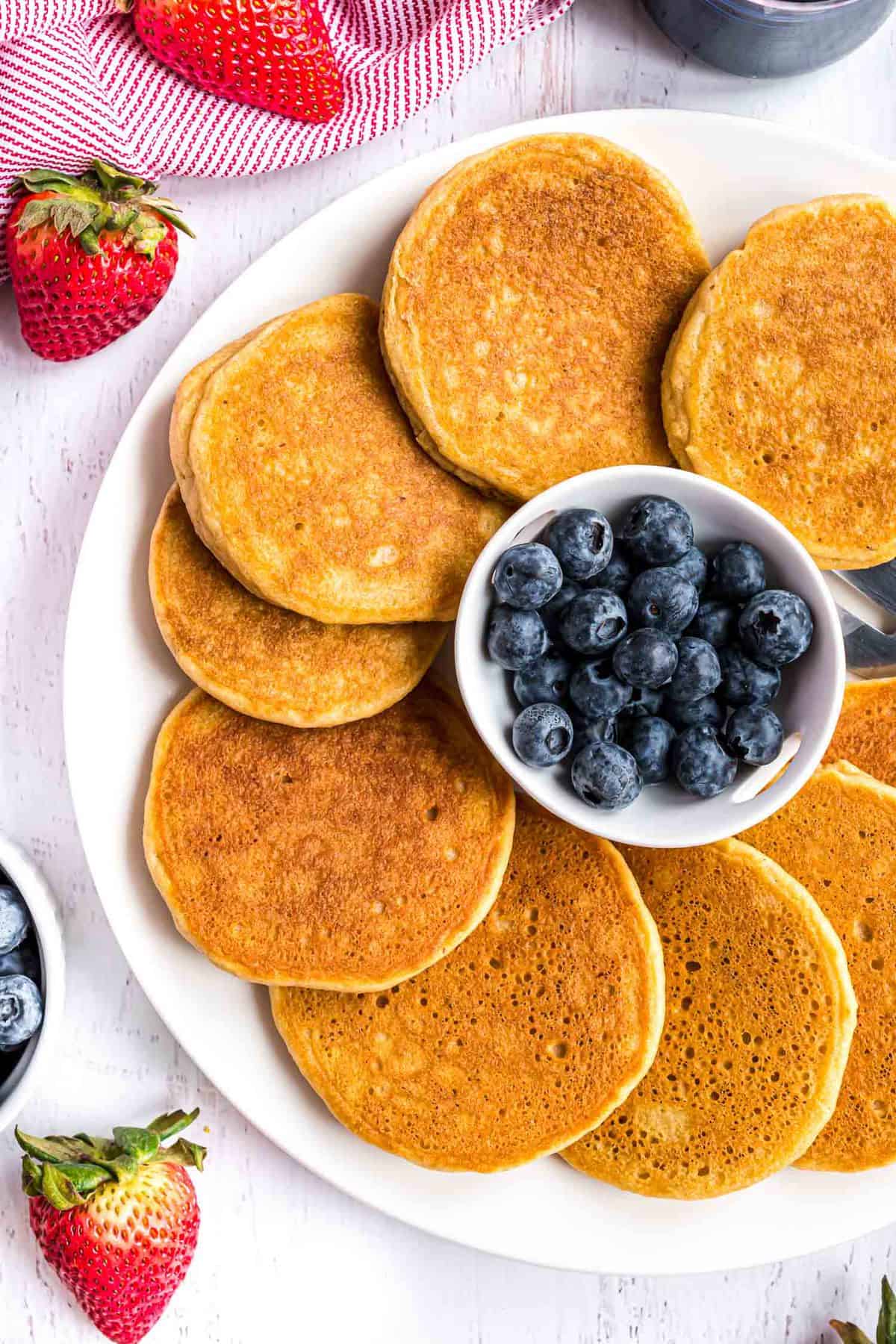 Vue de dessus de pancakes sur un plateau entouré d'un bol de myrtilles.