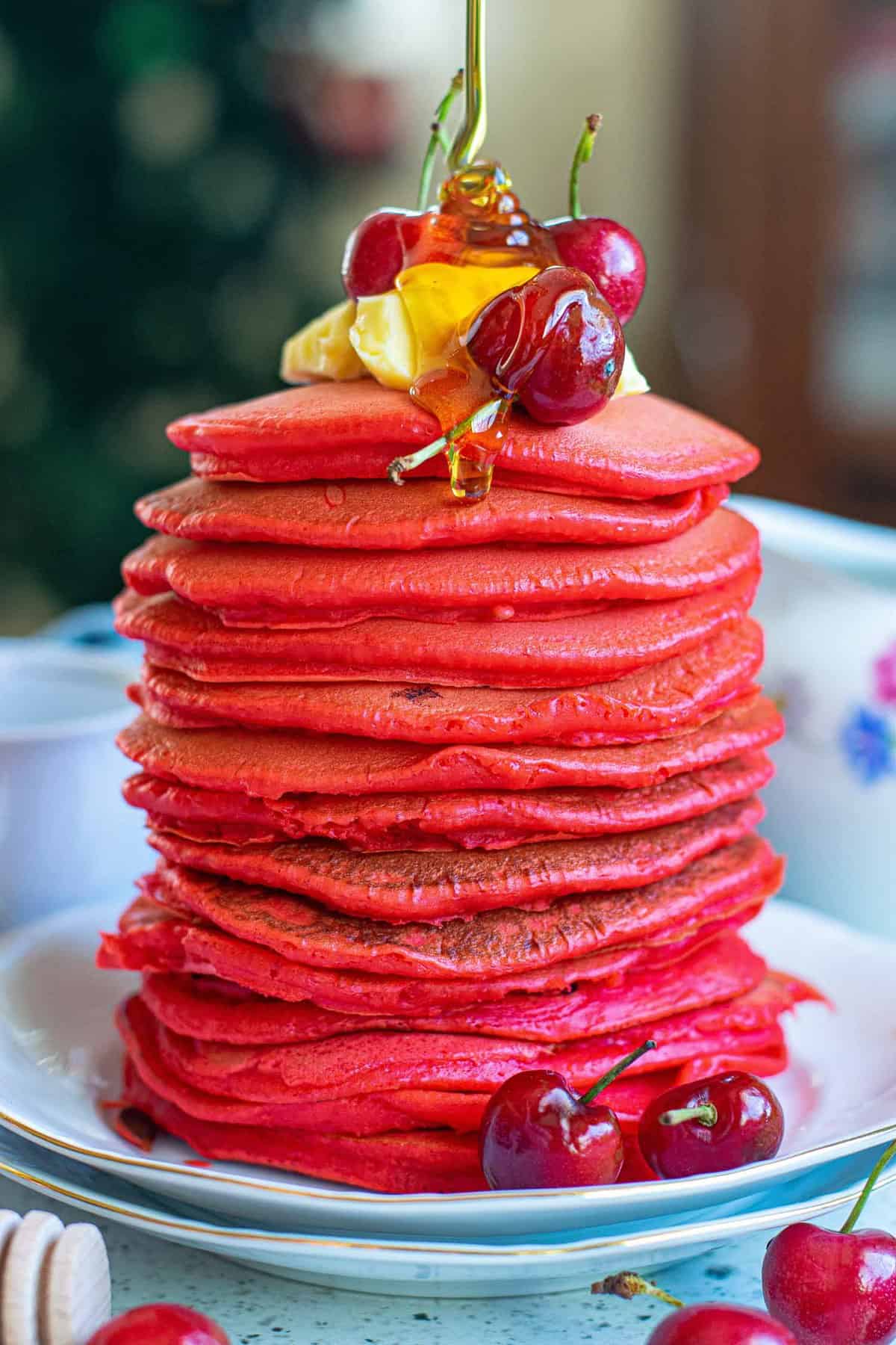 Du miel versé sur une grande pile de pancakes rouges.