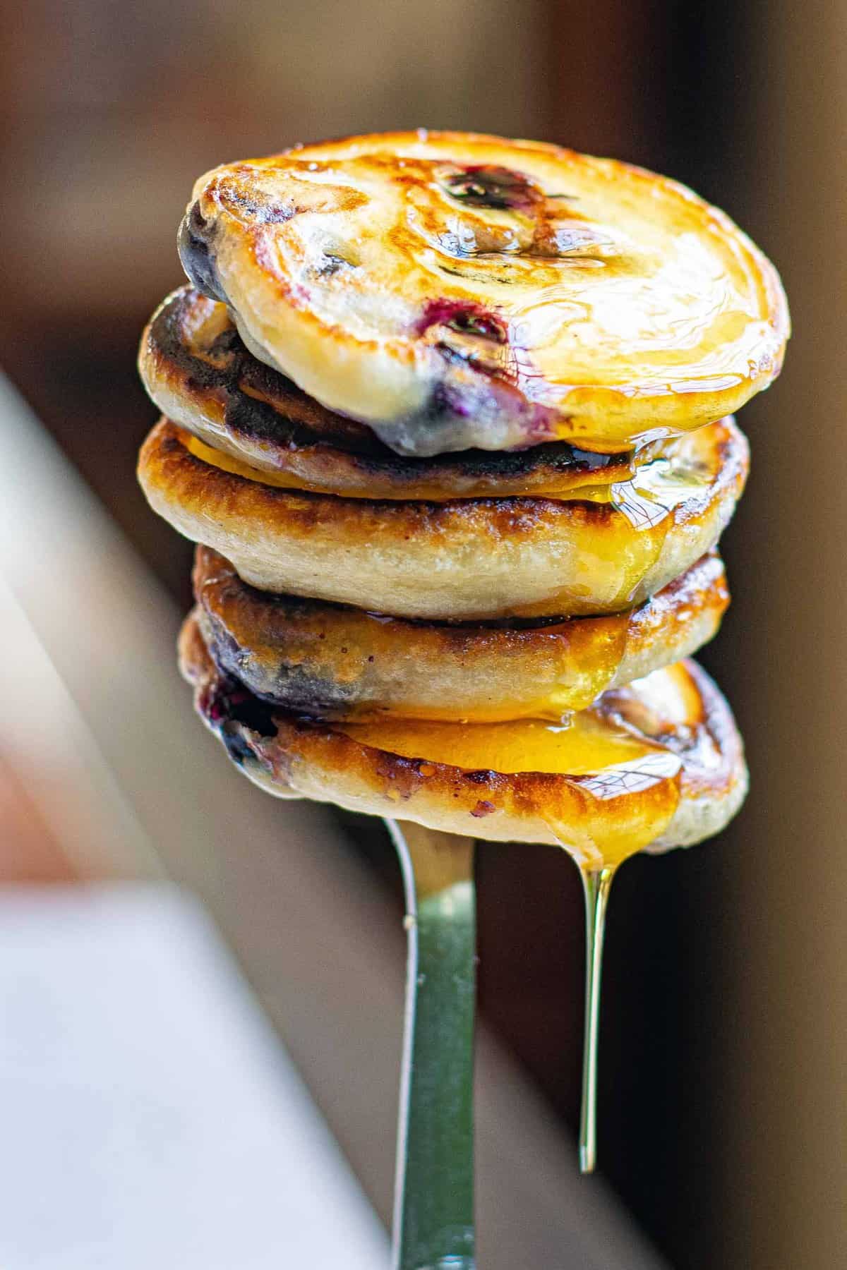 Une pile de petits pancakes végan aux myrtilles sur une fourchette, dégoulinant de sirop.