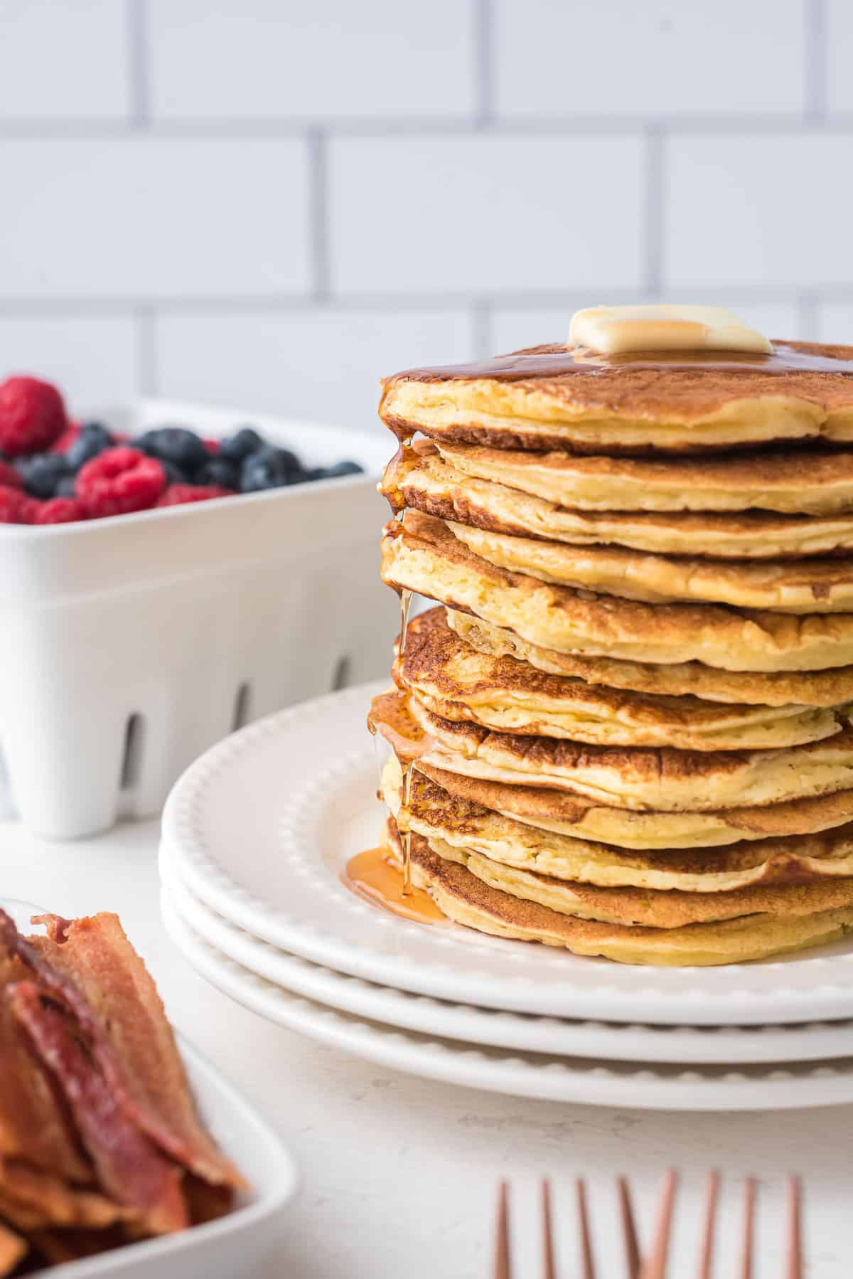 Très haute pile de pancakes garnis de beurre et dégoulinant de sirop d'érable.