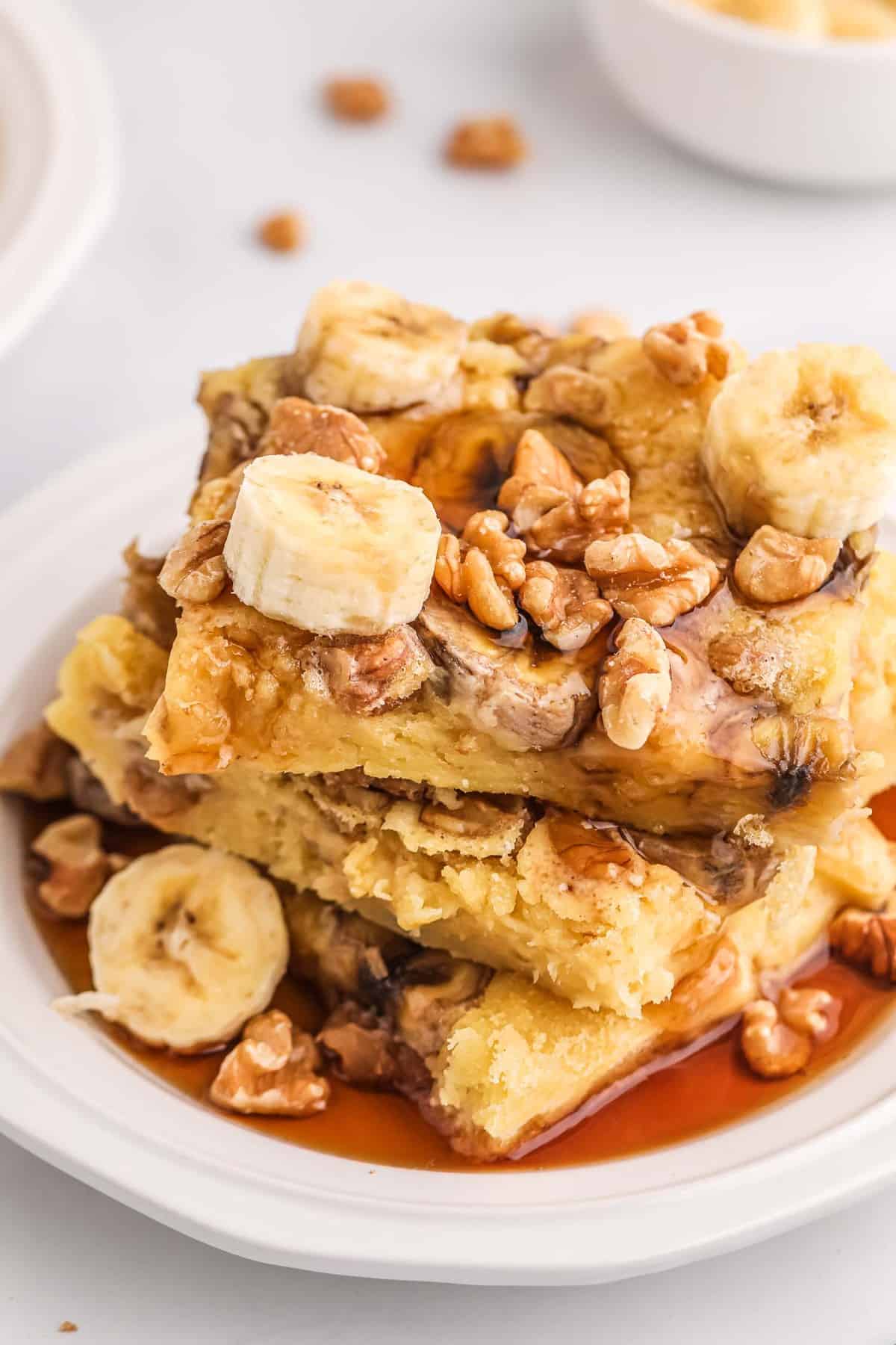 Une pile de pancakes carrés garnis de tranches de banane, de noix et de sirop.