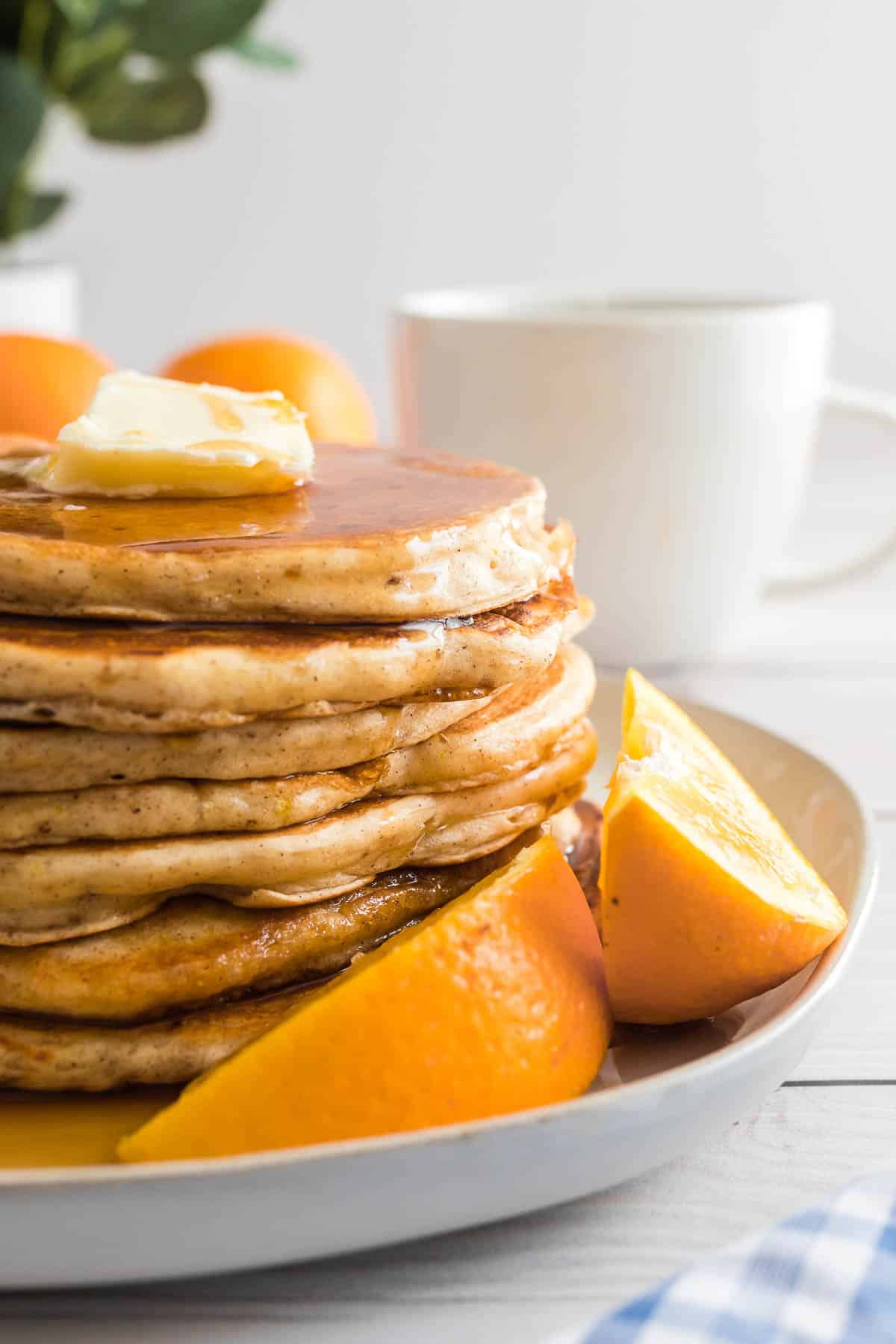 Tas de pancakes à l'orange sur une assiette avec des quartiers d'orange.