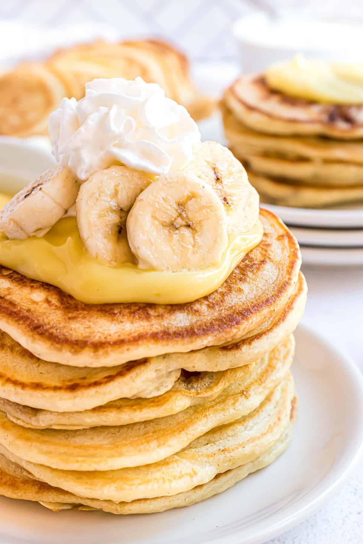 Gros plan d'une pile de pancakes garnie de pudding, de crème fouettée et de bananes.