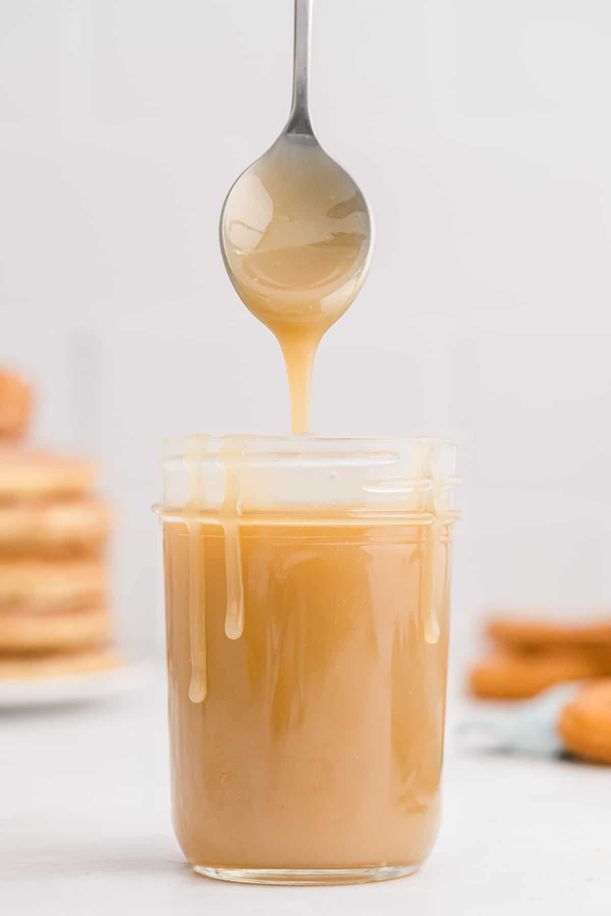 Caramel dans un pot, coulant sur les côtés du pot, une cuillère en suspension au-dessus.